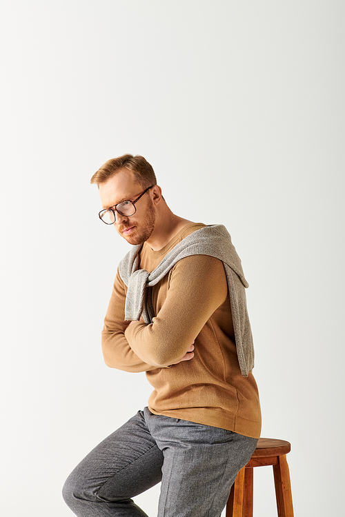 A stylishly attired man confidently perched atop a wooden stool.