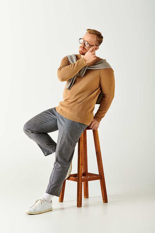 Handsome man in stylish attire sitting on top of a wooden stool.