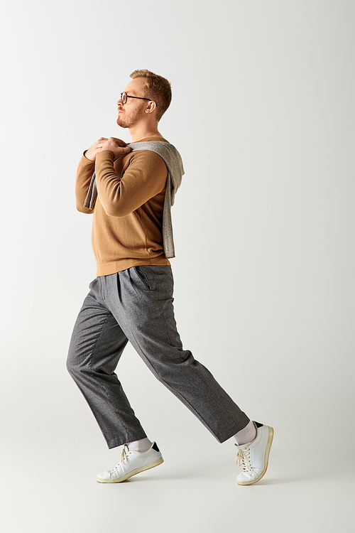 A stylish man wearing a brown sweater walks gracefully.