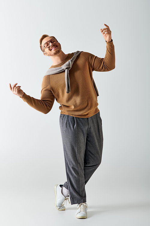 Handsome man in brown sweater and gray pants striking a pose.