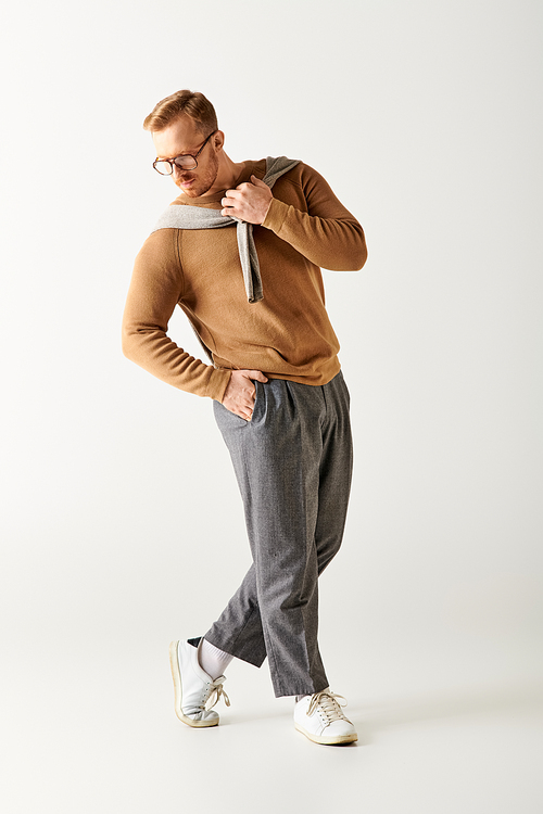 Handsome man in a brown sweater and grey pants striking a stylish pose.