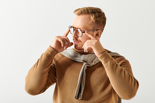 Handsome man in brown sweater holds his glasses.