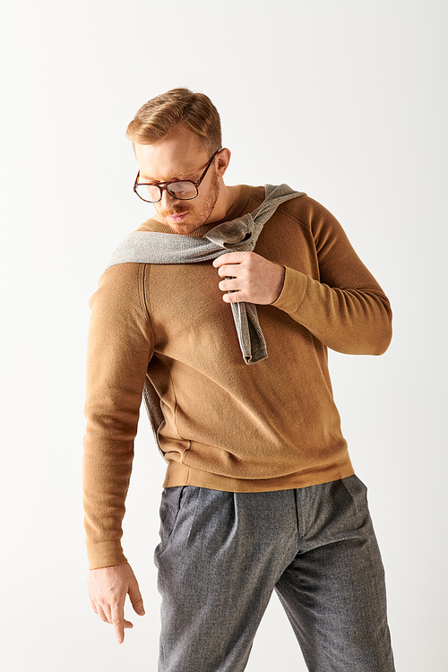 A stylish man wearing glasses and a sweater poses confidently.