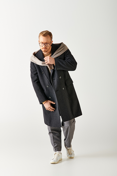 A dapper man in a coat and glasses confidently poses for a portrait.