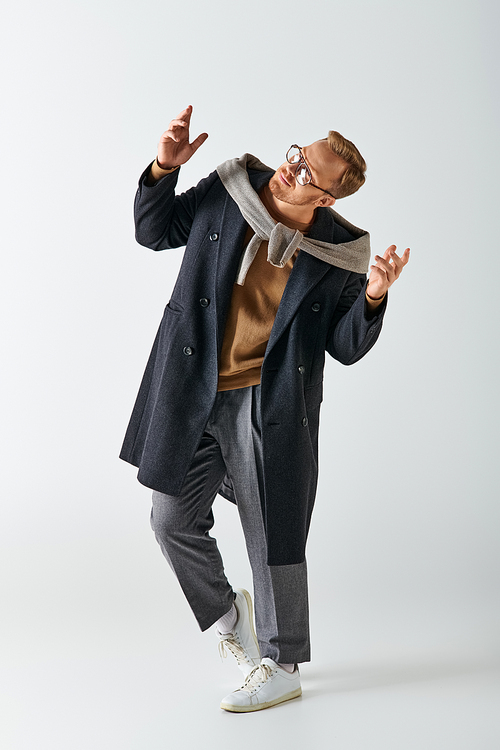 A stylish man in a coat and glasses energetically dances.