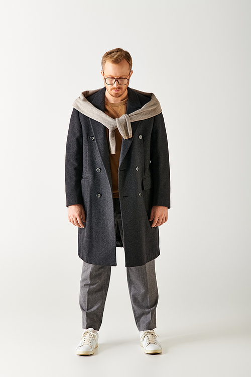 Handsome man in coat and sweater posing in front of white backdrop.