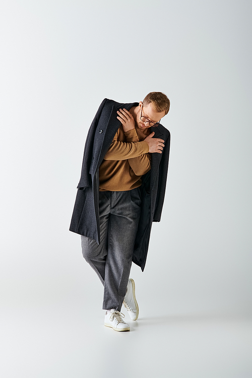 A stylish man poses confidently in a brown shirt and black coat.