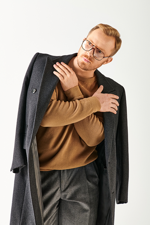 A fashionable man in glasses and a coat posing confidently for a portrait.