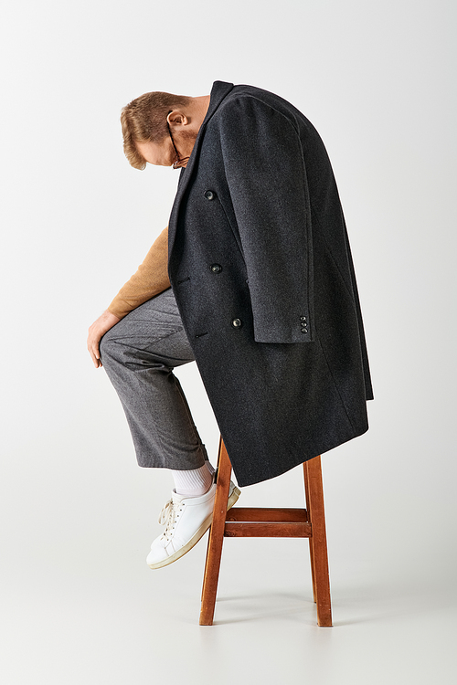 Stylish man confidently sits atop a wooden chair.