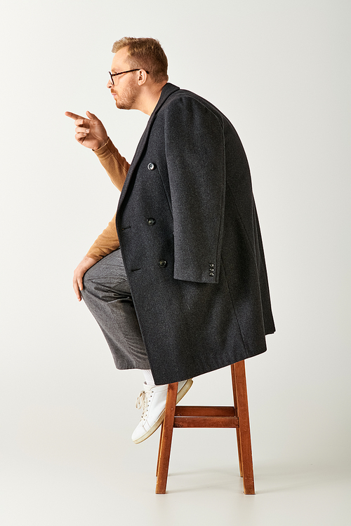 Stylish man sitting atop wooden stool with poise.