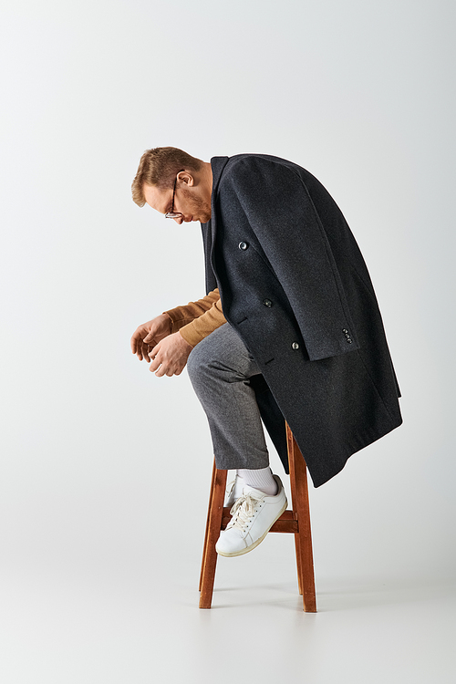 A handsome man in stylish attire confidently sits on top of a wooden chair.