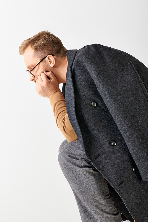 Stylish man in suit and glasses leans against a wall.