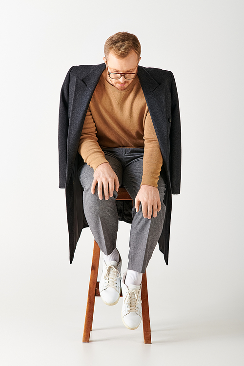 A handsome man in stylish attire poses actively while sitting on top of a wooden chair.