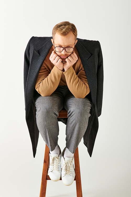 Stylish man sits on wooden chair, exuding confidence.