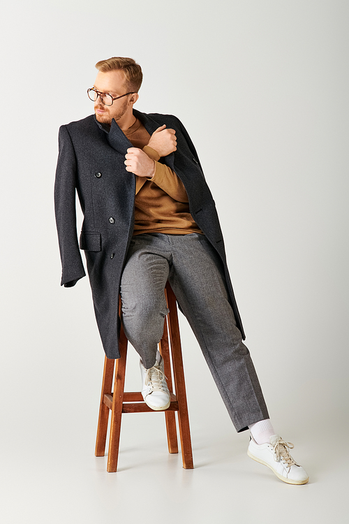 Handsome man in stylish attire, actively posing on a wooden stool.