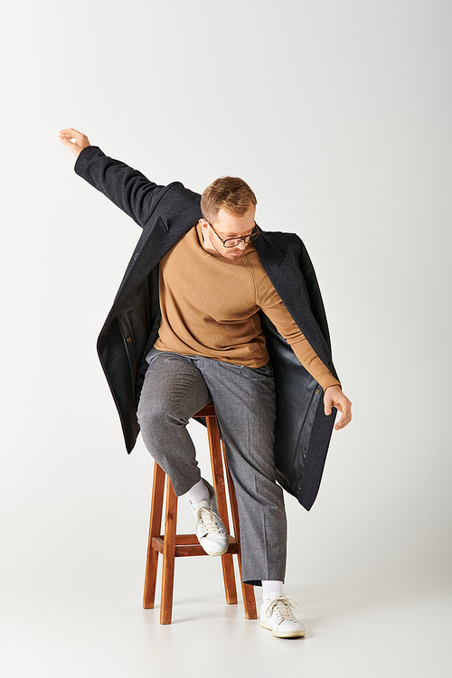 Handsome man in fashionable attire sits confidently on a wooden stool.