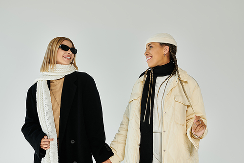 A joyful moment between two women dressed warmly for autumn, smiling and holding hands together.