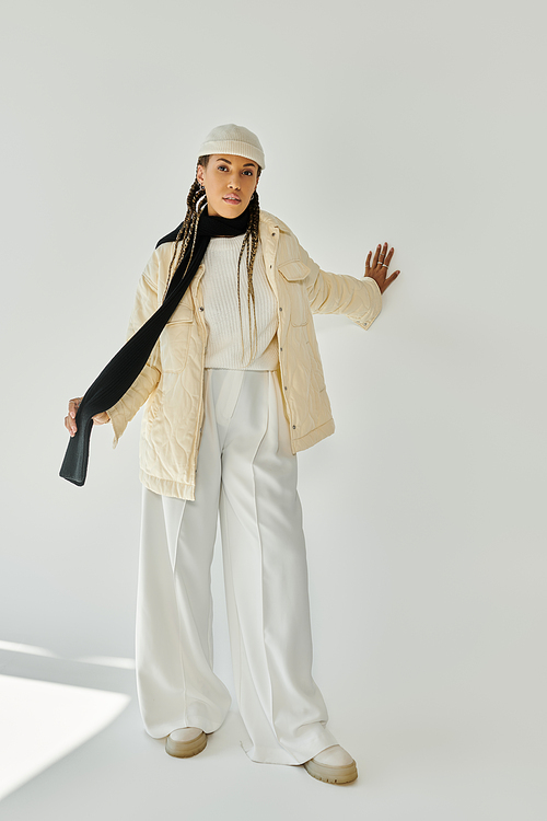 Attractive young woman in stylish warm attire posing on white backdrop.