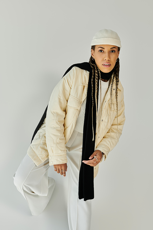 Trendy young woman in stylish warm attire posing on white backdrop.