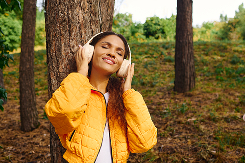 A young African American woman embraces the autumn landscape while hiking, surrounded by colorful trees.