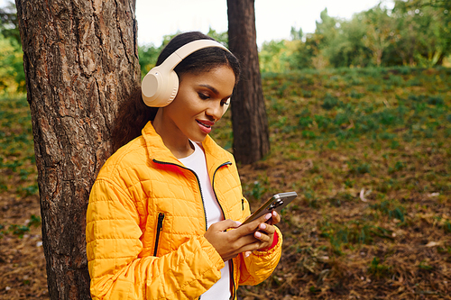 A young woman embraces nature while checking her phone in a colorful autumn forest.