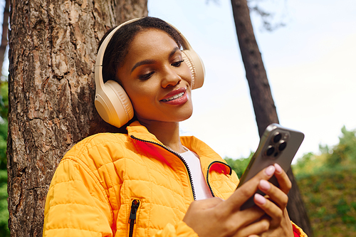 Amidst the colorful autumn trees, a young woman smiles while checking her phone on a hiking trail.