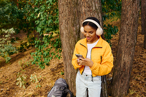 A young African American woman checks her phone while hiking through a colorful autumn forest.