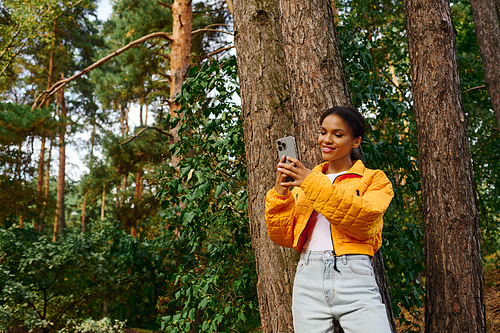 A young African American woman enjoys her time hiking, surrounded by autumn colors in a forest.