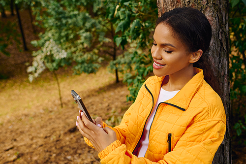 Amidst the colorful autumn foliage, a young woman engages with her phone, soaking in nature beauty.