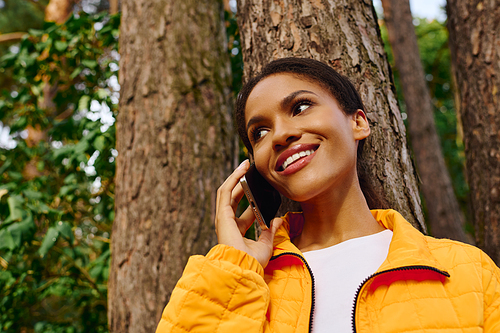 A young African American woman smiles brightly as she chats on her phone during an autumn hike.