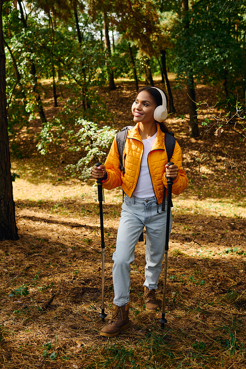 A young African American woman embraces the beauty of autumn while hiking through a serene forest trail.