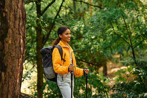 A young African American woman enjoys her hiking journey through a colorful autumn forest, embracing nature.