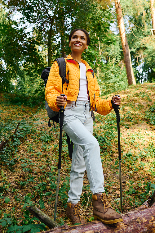 A young African American woman confidently hikes through a colorful autumn forest, embracing nature beauty.