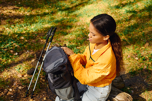 A young African American woman enjoys her hike through a colorful forest, fully immersed in nature's charm.