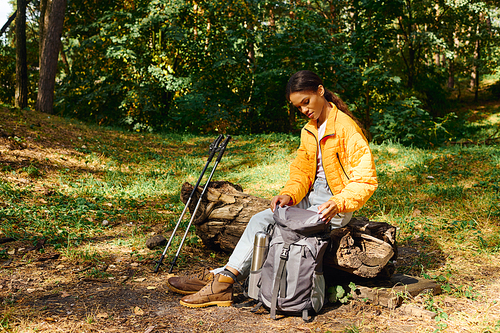 A determined young woman explores a vibrant forest, adjusting her gear amidst the autumn foliage.