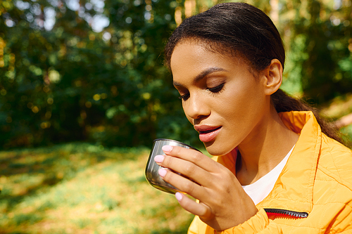 In a colorful autumn forest, a young woman savors a warm drink during her hiking adventure.