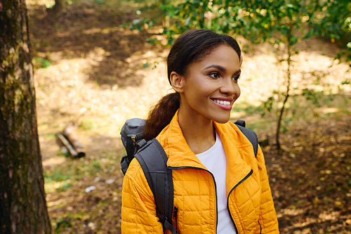 A cheerful young woman in a bright jacket explores the colorful forest during her autumn adventure.