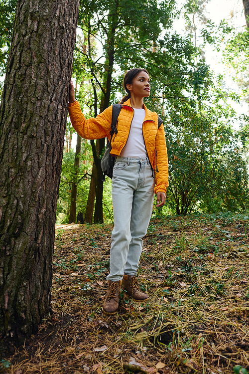 A young African American woman stands confidently in an autumn forest, enjoying her hiking adventure.