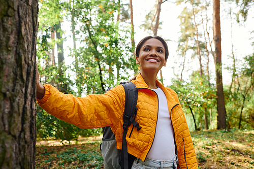 A young African American woman enjoys an autumn hike, embracing nature beauty in the colorful forest.