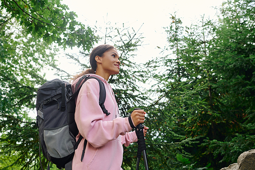 A young African American woman enjoys her hike through a colorful autumn forest, embracing nature beauty.