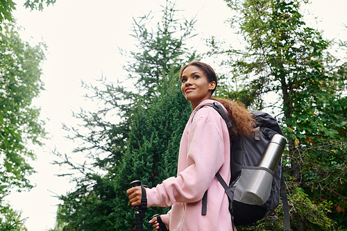 A young African American woman enjoys an energizing hike in a colorful autumn forest surrounded by nature.