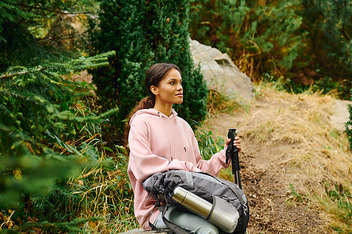 A young African American woman pauses while hiking through a colorful autumn forest, taking in the surroundings.