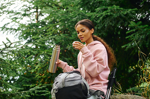 A young African American woman takes a moment to savor tea amidst colorful autumn foliage.