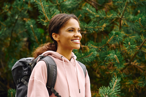 A young African American woman smiles brightly while hiking through a colorful autumn forest trail.