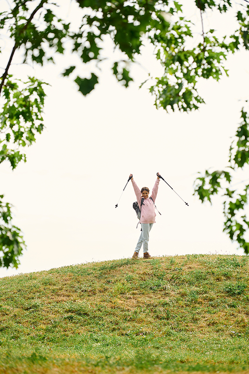 A joyful young woman triumphantly raises her arms while hiking on a hill surrounded by autumn colors.