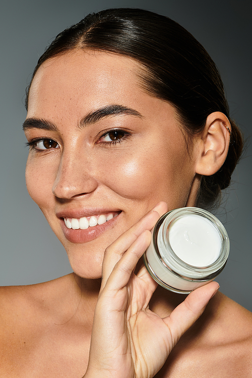 A smiling woman proudly presents her favorite skincare cream, glowing in natural light.