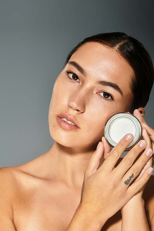 The beautiful woman gently showcases a skincare jar while highlighting her flawless complexion.