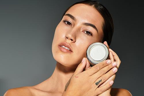 A woman gently holds a skincare jar while highlighting her glowing complexion in warm lighting.