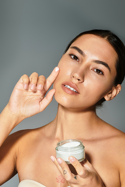 The woman gently applies cream to her face, showcasing her beauty and skincare routine.