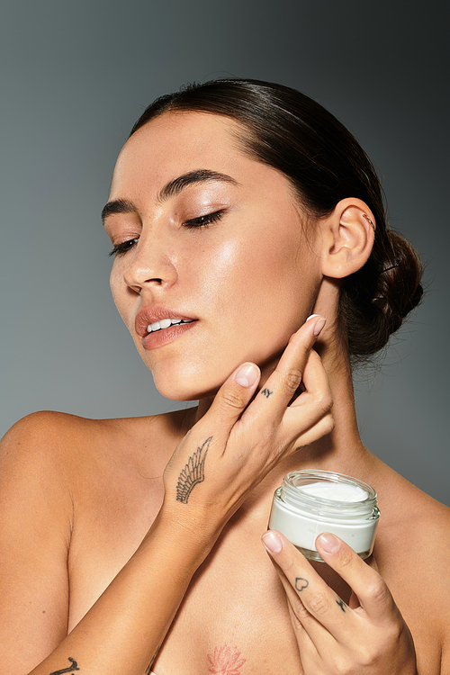 A woman gently applies cream to her skin with a thoughtful expression in a studio.